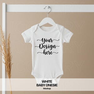 Puede incluir: Maqueta de body de bebé blanco con el texto "Your Design Here" en fuente cursiva negra.