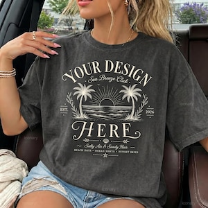 May include: A charcoal gray short-sleeve t-shirt featuring a cream-colored graphic print. The design includes the text "YOUR DESIGN HERE", "Sea Breeze Club", "EST. 2026", and "Salty Air & Sandy Hair" with illustrations of palm trees and a sunset.