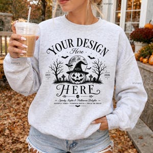 May include: A light gray crewneck sweatshirt featuring a black graphic print of a jack-o'-lantern wearing a witch hat, bare trees, a full moon, and the text "YOUR DESIGN HERE" with "EST. 2026" and "Spooky Nights & Halloween Delights" below.