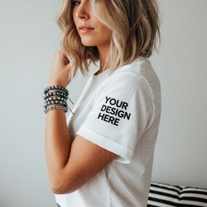 May include: White t-shirt with short sleeves and a black text design on the left sleeve that says "YOUR DESIGN HERE".