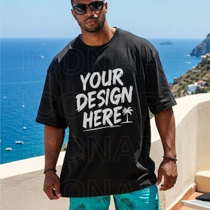 May include: Black t-shirt with the text "YOUR DESIGN HERE" in white. The shirt has a relaxed fit and short sleeves. A palm tree graphic is below the text. The person is wearing sunglasses and blue shorts.