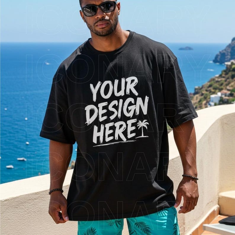 May include: Black t-shirt with the text "YOUR DESIGN HERE" in white. The shirt has a relaxed fit and short sleeves. A palm tree graphic is below the text. The person is wearing sunglasses and blue shorts.