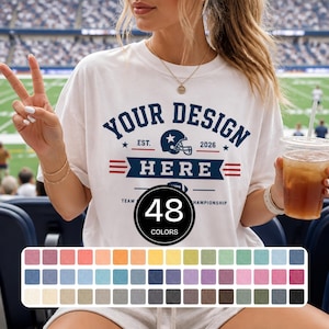 May include: A white t-shirt featuring dark blue text that reads YOUR DESIGN HERE, with a football helmet icon, the text EST. 2026, and a graphic of a football. Below the design is a circular badge stating 48 COLORS, followed by a grid of 48 colour swatches.