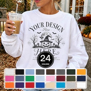 Op de afbeelding: Een wit sweatshirt met lange mouwen en een zwarte grafische print van een pompoen met een heksenhoed, omringd door bomen, vleermuizen en grafstenen, met de tekst "YOUR DESIGN Here" en "EST. 2026" boven en onder de illustratie gedrukt.