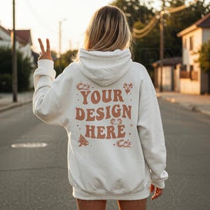 以下が含まれることがあります： 背面に「YOUR DESIGN HERE」と書かれた茶色のデザインが施された白いパーカー