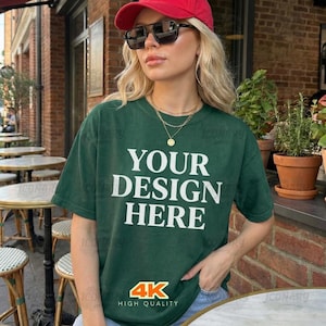 May include: A dark green t-shirt with the text "YOUR DESIGN HERE" in white. The shirt is worn with a red baseball cap and sunglasses. The image also includes a "4K HIGH QUALITY" logo.