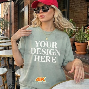 Może przedstawiać: Jasnozielona koszulka z białym napisem "YOUR DESIGN HERE". Na zdjęciu widoczna jest również czerwona czapka z daszkiem, okulary przeciwsłoneczne i złote naszyjniki. Obraz ma logo 4K wysokiej jakości.