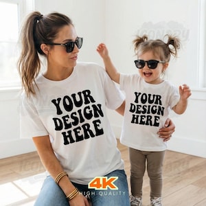 Op de afbeelding: Een vrouw en een kind dragen bijpassende witte t-shirts met de tekst "YOUR DESIGN HERE" in het zwart. Beiden dragen een zonnebril. De vrouw draagt een blauwe spijkerbroek en gouden armbanden. Het kind draagt een bruine broek en grijze sneakers. De afbeelding heeft een "4K HIGH QUALITY" logo.