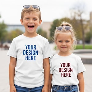 Może przedstawiać: Dwoje dzieci w białych koszulkach z napisem "YOUR DESIGN HERE" w kolorze niebieskim i bordowym. Chłopiec uśmiecha się z okularami przeciwsłonecznymi na głowie, a dziewczynka uśmiecha się z okularami przeciwsłonecznymi na głowie. Stoją na zewnątrz.