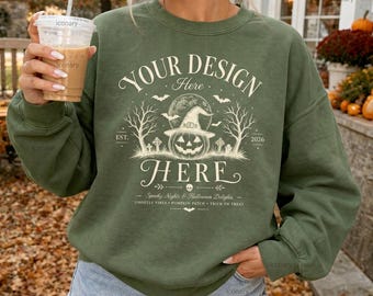 May include: An olive green crewneck sweatshirt featuring a cream-coloured graphic of a jack-o'-lantern wearing a witch hat, surrounded by bare trees, bats, and tombstones. The text reads YOUR DESIGN HERE, EST. 2026, Spooky Nights & Halloween Delights.