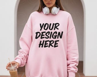 Könnte beinhalten: Ein hellrosa Sweatshirt mit dem Text "YOUR DESIGN HERE" in Schwarz. Das Sweatshirt wird mit einer rosa Kappe und weißen Kopfhörern getragen. Eine transparente Plastikbecher mit einem Strohhalm wird in der Hand gehalten.