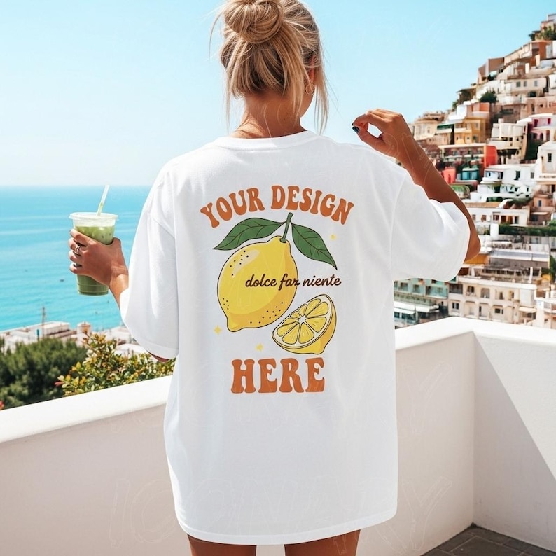 May include: White t-shirt with a lemon graphic and the text "YOUR DESIGN dolce far niente HERE". The design features a whole lemon and a lemon slice with green leaves. The shirt is worn outdoors.