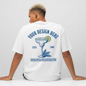 May include: White t-shirt with a blue margarita design on the back. The design includes the text "YOUR DESIGN HERE", "ESTD 1980", and a margarita glass with a lime wedge. Below the margarita glass is a list of text.