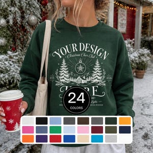 Könnte beinhalten: Ein dunkelgrünes Sweatshirt mit Rundhalsausschnitt und einem weißen Grafikdruck mit dem Text "YOUR DESIGN HERE" und "Christmas Cheer Club". Das Design zeigt Illustrationen von Tannenbäumen, einem Haus und einer Schneeflocke. Eine Farbkarte ist sichtbar.