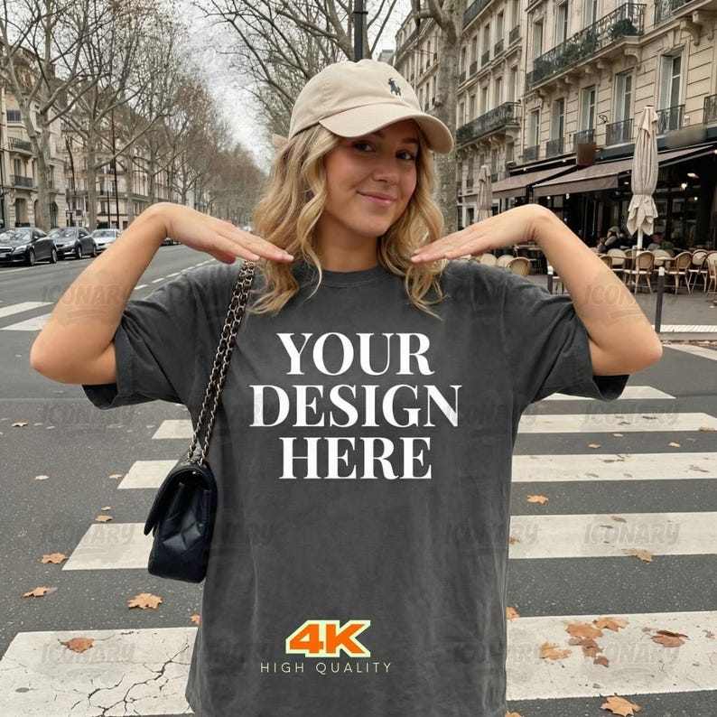 May include: Dark gray t-shirt with the text "YOUR DESIGN HERE" in large white letters. The shirt also has a "4K HIGH QUALITY" logo. The person in the image is wearing a beige baseball cap and carrying a black purse.