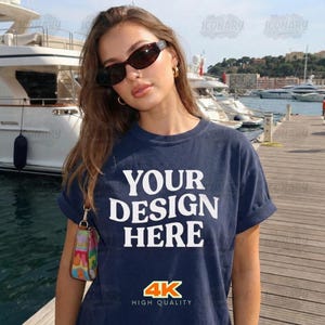 May include: A navy blue t-shirt with the text "YOUR DESIGN HERE" in white block letters. The shirt also features the text "4K HIGH QUALITY" in yellow and red. The person is wearing sunglasses and gold earrings.