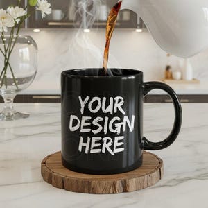 May include: A black ceramic mug with the text "YOUR DESIGN HERE" in white, steam rising as coffee is poured into it. The mug sits on a wooden coaster. The background shows a kitchen setting.