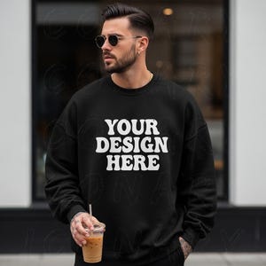 Könnte beinhalten: Schwarzes Sweatshirt mit dem weißen Text "YOUR DESIGN HERE". Das Sweatshirt hat einen Rundhalsausschnitt. Die Person auf dem Bild trägt eine Sonnenbrille und hält einen transparenten Plastikbecher mit Strohhalm.