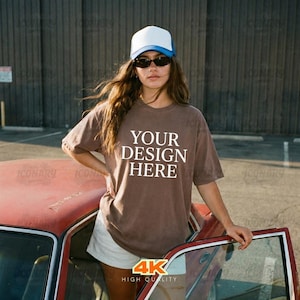 May include: A brown t-shirt with the text "YOUR DESIGN HERE" in white. The person in the image is wearing a white and blue trucker hat and sunglasses. The image is labeled "4K HIGH QUALITY".
