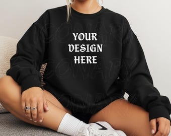 May include: Black crewneck sweatshirt with the text "YOUR DESIGN HERE" in a white, gothic-style font. The sweatshirt is a solid black color. The model is wearing white sneakers and socks.