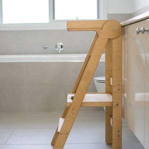 May include: A wooden step stool with two steps and a top platform. The stool is made of light wood and has a simple design.