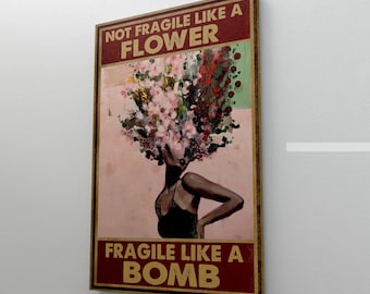 Puede incluir: Impresión artística enmarcada que representa a una mujer con un tocado floral. El texto dice "NOT FRAGILE LIKE A FLOWER, FRAGILE LIKE A BOMB" en letras doradas sobre un fondo granate. La mujer lleva un top negro.