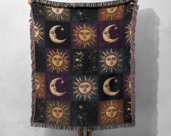 Può includere: Una coperta tessuta con un motivo ripetuto di soli e lune crescenti in quadrati. La coperta ha un bordo a frange ed è principalmente nelle tonalità dell'oro, del viola e del nero. Il design celeste aggiunge un tocco mistico all'arredamento.