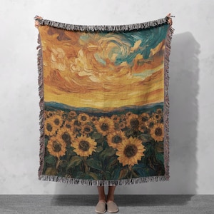 May include: A woven throw blanket featuring a painting of a field of sunflowers under a swirling sky. The colors are yellow, orange, blue, and green.