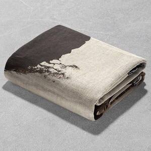 May include: A folded brown and beige throw blanket with a black and white abstract design. The blanket is folded in half and the design is visible on the top half of the blanket.