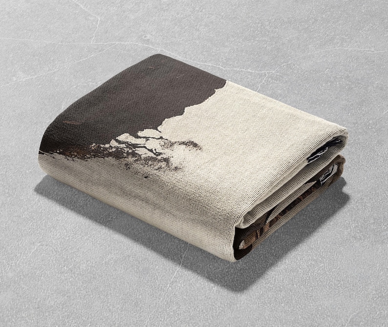 May include: A folded brown and beige throw blanket with a black and white abstract design. The blanket is folded in half and the design is visible on the top half of the blanket.