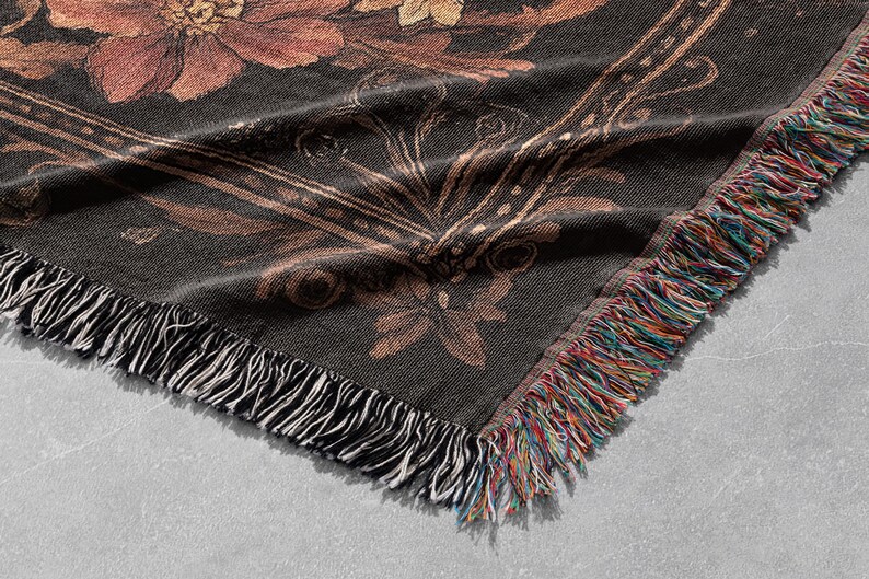May include: A black woven throw blanket with a floral pattern in shades of brown and gold. The blanket has a fringe border.