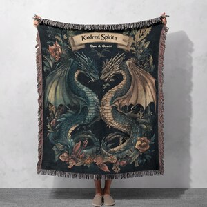 Könnte beinhalten: Eine gewebte Wanddecke aus Tapisserie mit dunklem Hintergrund, die zwei ineinander verschlungene Drachen mit floralen Akzenten zeigt. Der Text "Kindred Spirits" ist in einem Banner über den Drachen dargestellt, mit den Namen "Dan & Grace" darunter.