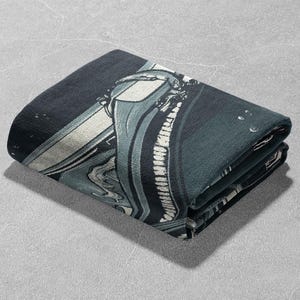 May include: A folded dark blue and white throw blanket with a graphic print of a spaceship. The blanket has a textured surface.
