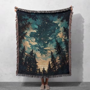 May include: A woven throw blanket featuring a starry night sky scene with silhouetted trees. The blanket has a dark blue and teal color palette with a fringed edge. The design depicts a forest with a view of the night sky.