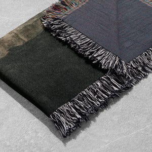 May include: A black and green woven throw blanket with a fringe border. The blanket is folded in half and the fringe is visible on both sides.