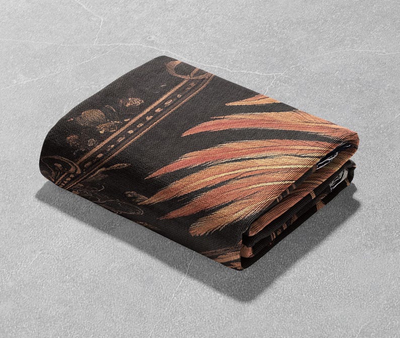 May include: A black and gold throw blanket with a feather pattern. The blanket is folded in half and has a textured surface.