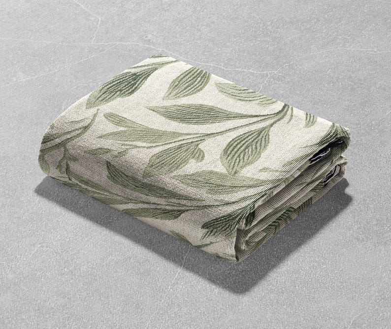 Op de afbeelding: Gevouwen deken met een botanisch bladerpatroon in groen- en cr&egrave;metinten. De bladeren zijn gedetailleerd en over de stof verdeeld. De deken is netjes opgevouwen en toont het patroon op de boven- en zijkanten.