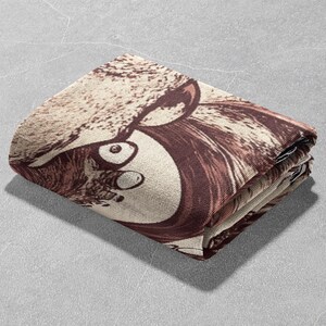 May include: A folded brown and beige throw blanket with a graphic print of a cartoon animal face with large eyes.