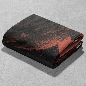 May include: Folded rectangular textile with a dark brown and red abstract design. The fabric appears to be a woven material, with the design visible on the top layer and the edges. The folded edges reveal a contrasting red color.