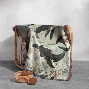 May include: A woven throw blanket with a green background and a pattern of whales and coral. The blanket is draped over a wicker chair.