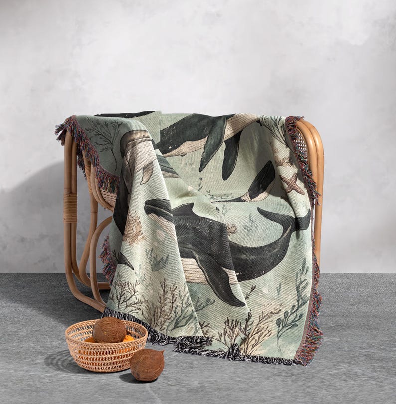 May include: A woven throw blanket with a green background and a pattern of whales and coral. The blanket is draped over a wicker chair.