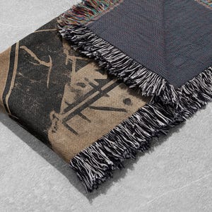 Pu&ograve; includere: Una coperta in tessuto intrecciato con una stampa grafica in bianco e nero e una frangia in bianco e nero. Il retro della coperta &egrave; di colore blu scuro.