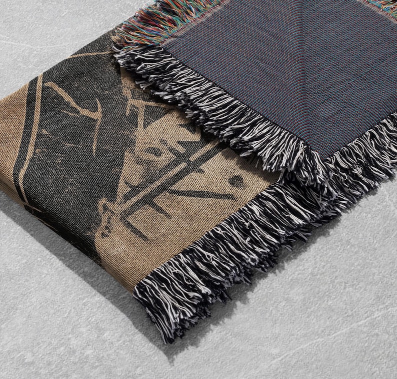 Pu&ograve; includere: Una coperta in tessuto intrecciato con una stampa grafica in bianco e nero e una frangia in bianco e nero. Il retro della coperta &egrave; di colore blu scuro.
