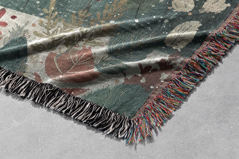 May include: A woven throw blanket with a botanical design. The blanket features a teal background with brown and white leaf and floral patterns. The edge is finished with a fringe of black and multicolored threads.