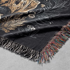 May include: Black and gold woven throw blanket with a fringed edge. The blanket features a floral design with a dark background.