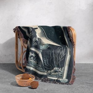 May include: A black and white woven throw blanket with a large shark and coral reef design. The blanket is draped over a wicker chair.