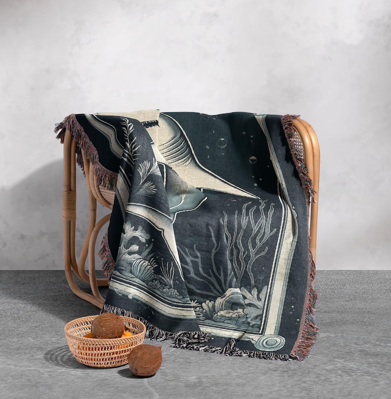 May include: A black and white woven throw blanket with a large shark and coral reef design. The blanket is draped over a wicker chair.