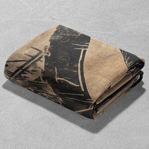 Pu&ograve; includere: Una coperta piegata di colore beige e nero con un design geometrico.