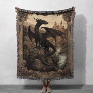 May include: A woven tapestry throw blanket featuring a black dragon with outstretched wings, perched on a rock in a woodland setting. A medieval castle is visible in the background.