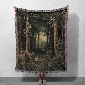 May include: A woven throw blanket featuring a detailed forest scene with tall trees, a Highland cow, and a fox resting among flowers. The rectangular textile has a dark green and brown colour palette with a decorative fringed edge on all sides.